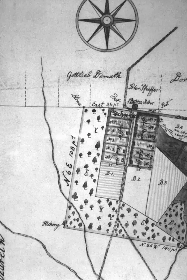 Black and white image showing detail from a hand-drawn 1776 map of Nazareth, showing the Schoeneck village lots and surrounding area. The "Gottes Acker" or God's Acre, is at the north end of Schoeneck. Houses on the lots are represented by a rectangle near the road. The Schul Haus now takes up lots eleven and twelve.