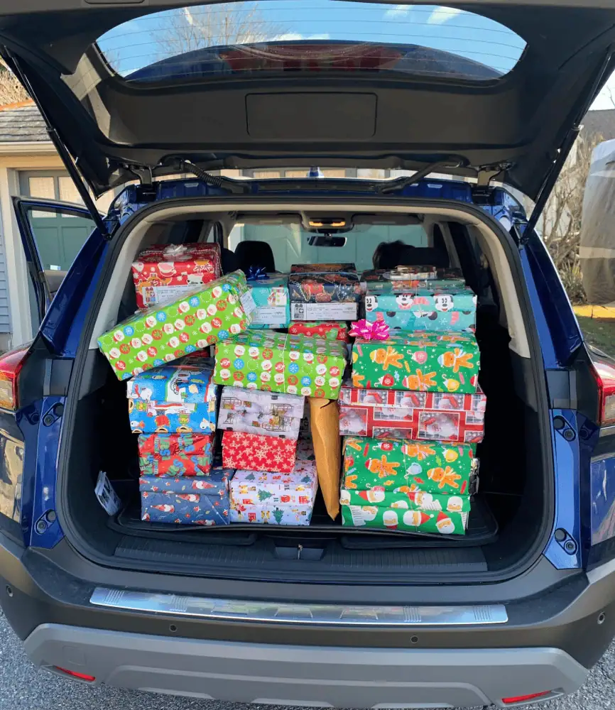 A photo shows the opened tailgate of an SUV. Inside the SUV are a festive pile of shoe boxes, each wrapped in a different Christmas wrapping paper.
