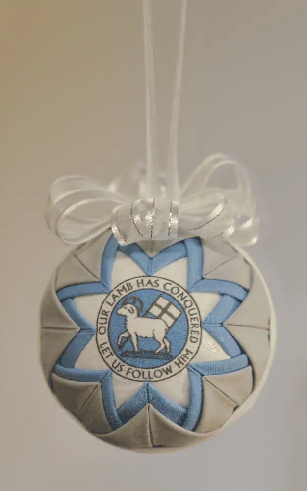 A round grey, white, and blue fabric ornament with an image of the Moravian Seal on the front.