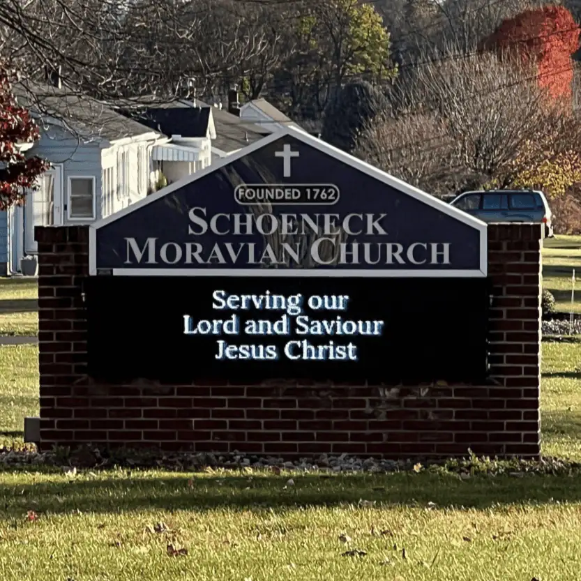 Schoeneck's Church sign - a brick enclosure for an LED sign. The top of the sign is a triangular shape with "Schoeneck Moravian Church - Founded 1762" written on it. The LED sign says, "Serving our Lord and Savior Jesus Christ."