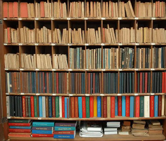 A photo of a large wooden shelf area with multiple shelves. The shelves have perhaps a hundred editions of past Moravian Daily Text books. Some of the books are look very old. Some of the books look more modern. Some of the books are thin and some are quite wide.