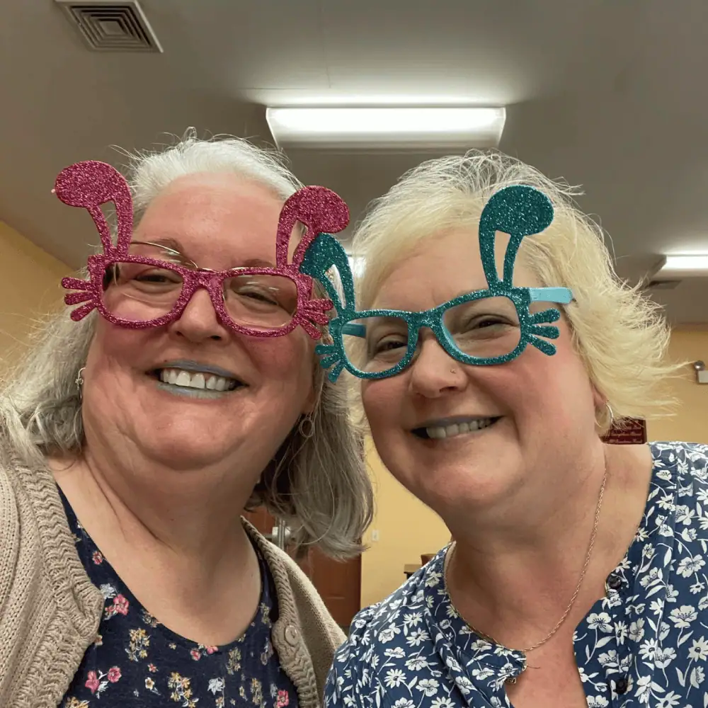 Two women, brave Schoeneckian youth group leaders, pose with big smiles while wearing funky, sparkly, pink and green plastic glasses.