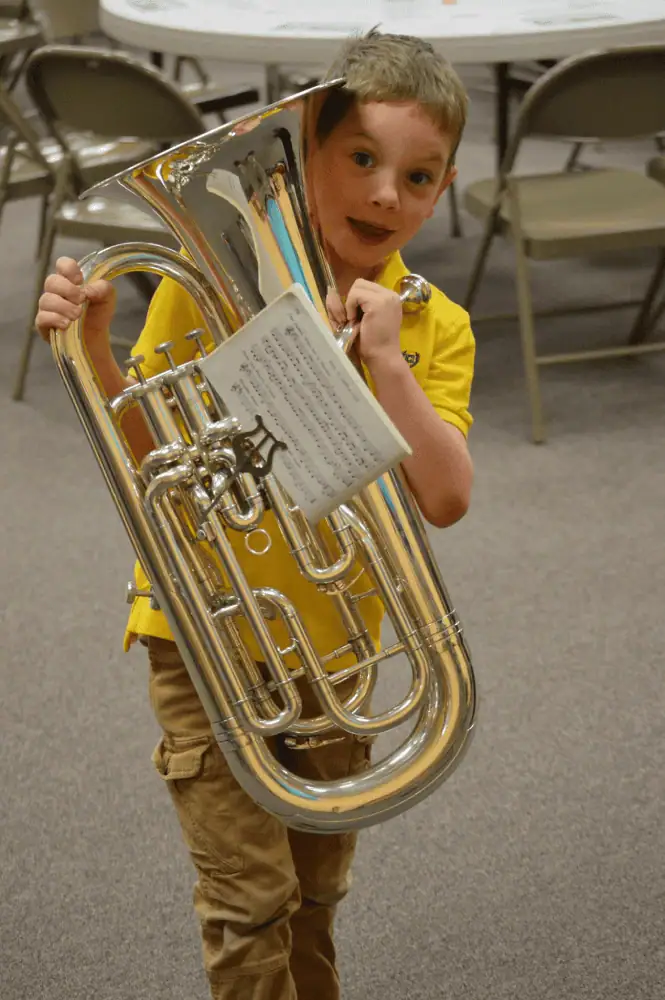A young boy holds a brass euphonium which is almost as big as he is!