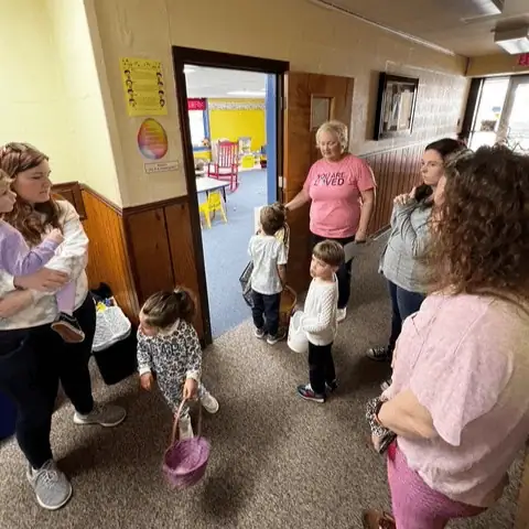 Several adults and children stand outside the church Nursery. The children are holding Easter baskets and eagerly awaiting the start of the annual Easter Egg Hunt.