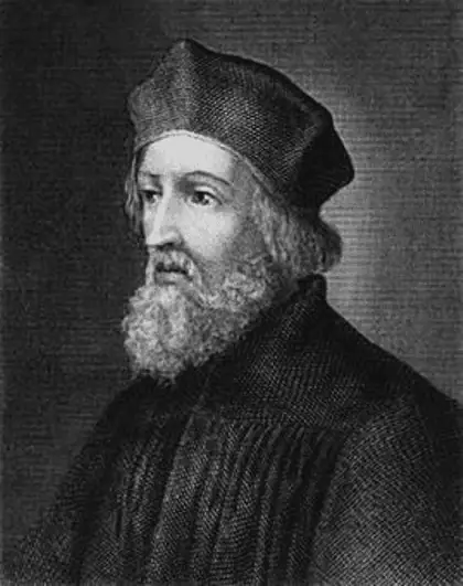 A black and white portrait engraving of John Hus. He is wearing a black soft rounded cap, possibly a coif commonly worn by scholars and clergy during that era. He has wide eyes, a long nose, and a curly grey beard. His robe is black.