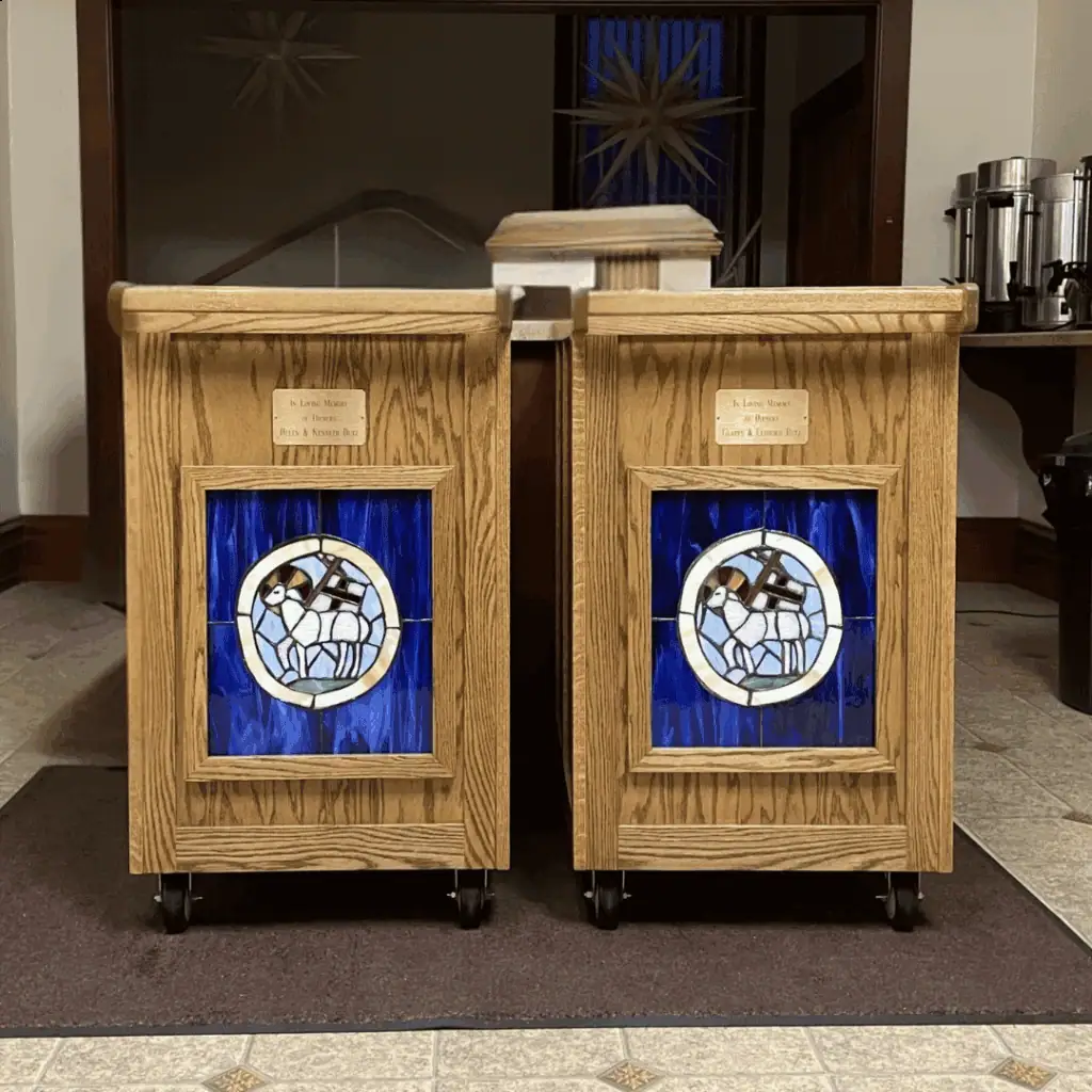 Two lovefeast carts in the Diener's Kitchen. The end of both carts feature a stained glass Agnus Dei and a brass dedication plaque.