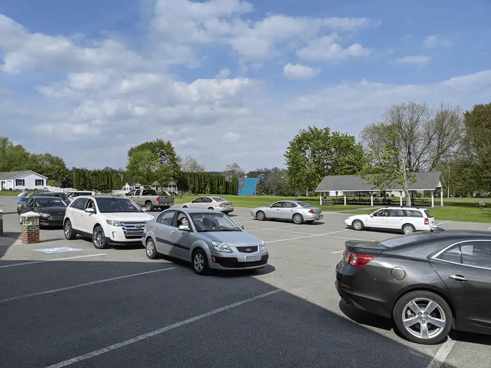 A photo showing two lines of cars in the parking lot on a sunny day. The line of cars in background are heading north, while the line in the foreground is heading south as they wait for the Mobile Pick-Up Community Dinner.
