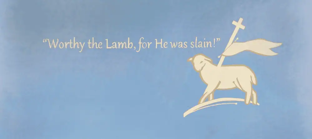 A photo of the wall in the Choir Room at Schoeneck Moravian Church. The wall is painted a light blue-grey with a modern Agnus Dei in a cream color with a golden-tan outline. Written in cream lettering is "Worthy the Lamb, for He was slain!"