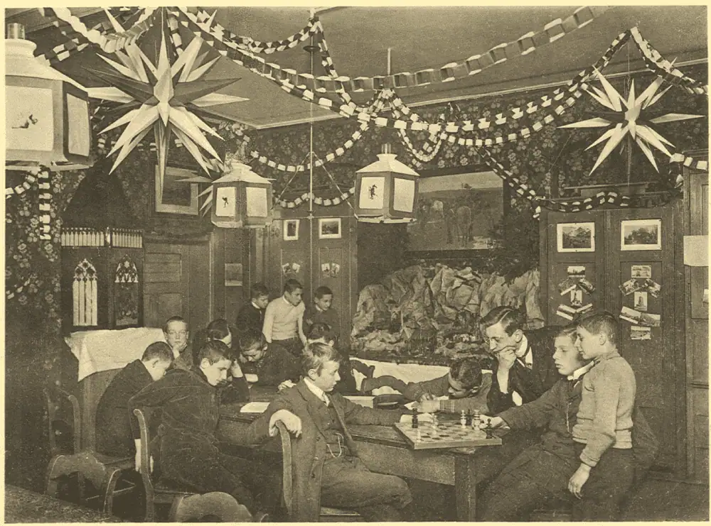 A black and white photo of boys sitting in a parlor decorated for Christmas with paper Moravian stars, garlands of paper rings, and a putz. The Moravian stars appear to have dark among the white points.