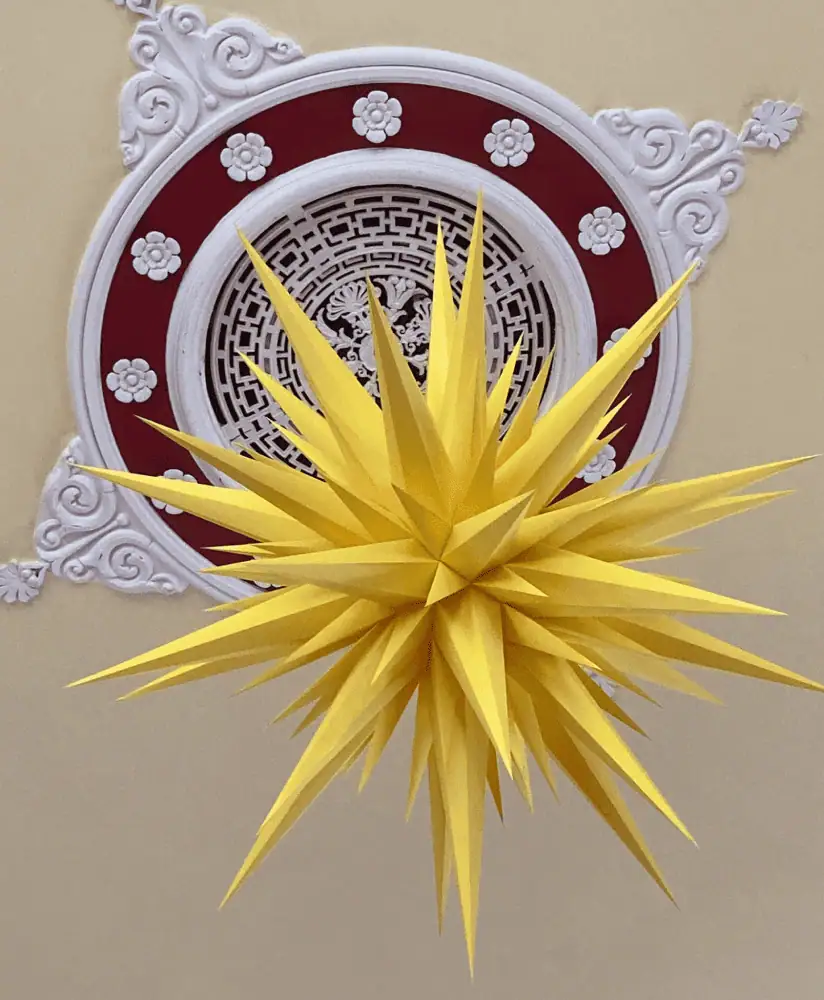 A yellow Moravian star hanging from an ornate burgundy and white plate on the ceiling of Ockbrook Moravian Church in Derby, United Kingdom.