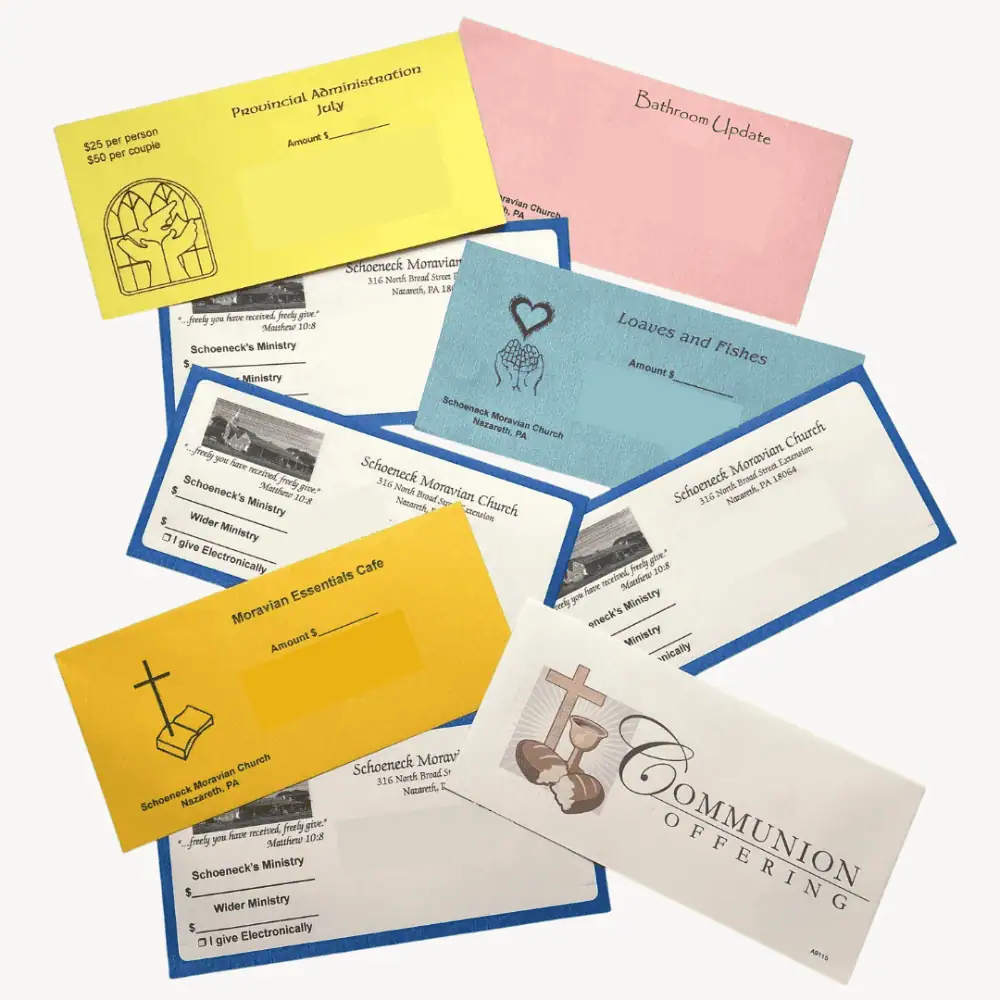 A photo of Schoeneck's offering envelopes which are mailed to the congregation each month. There are white envelopes with dark blue edges for weekly offerings, with a space to write in an amount for Schoeneck's Ministry and a space to write in an amount for Wider Ministry. In addition, there is a white Communion Offering envelope, a goldenrod envelope designated for Moravian Essentials Cafe, a pastel blue envelope designated for Loaves and Fishes, a pastel yellow envelope designated for Provincial Administration, and a pastel pink envelope designated for Bathroom Update.