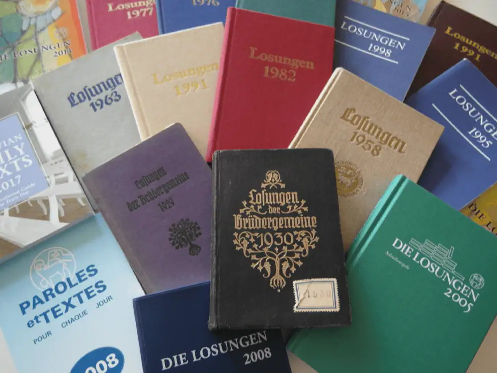 A photo showing past international editions of the Moravian Daily Texts, spread out in a fan pattern the books are in different colors with different language and from years as varied as 2005, 1930, 1963, 1995, 2017, etc.