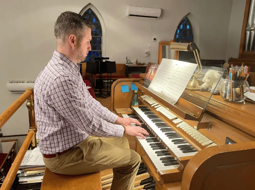 A photo of Ryan Morrow, Schoeneck's Director of Music Ministries, sitting at the organ console practicing a piece of music.