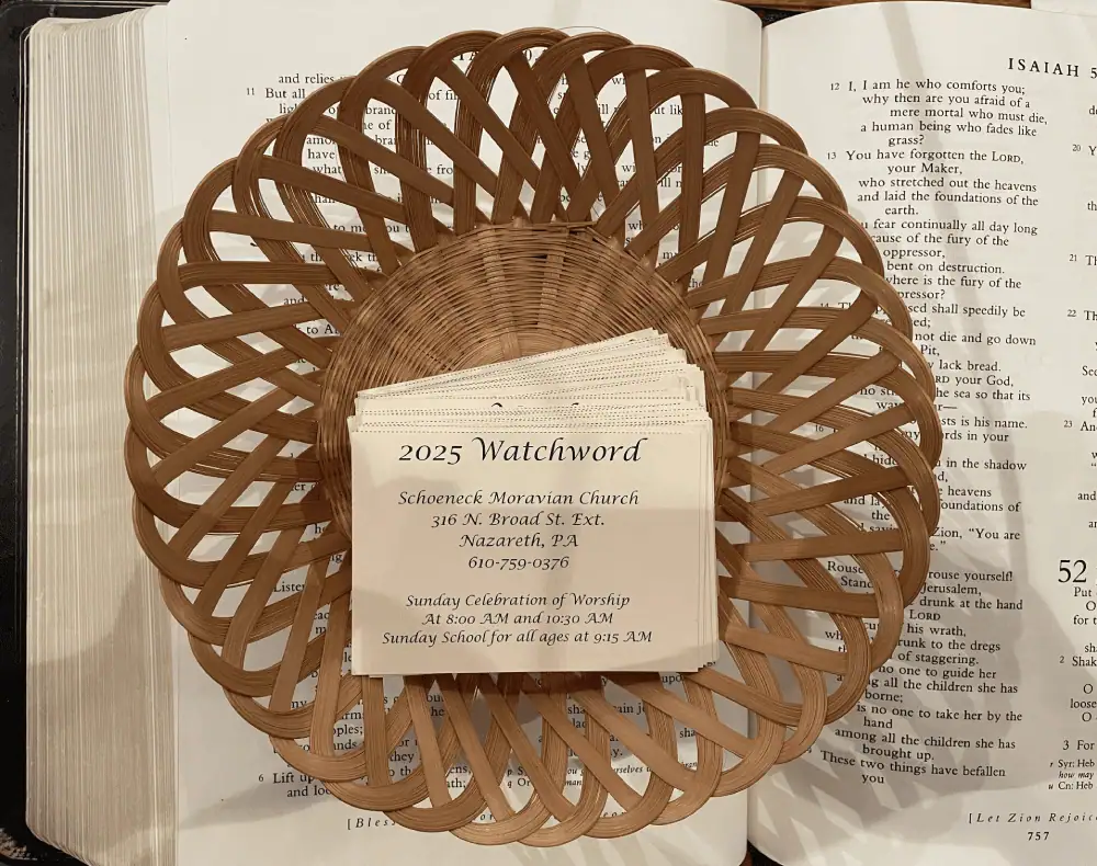 A basket sits on top of a large open Bible. Inside the basket are a pile of cards with the words "2025 Watchword" on them.