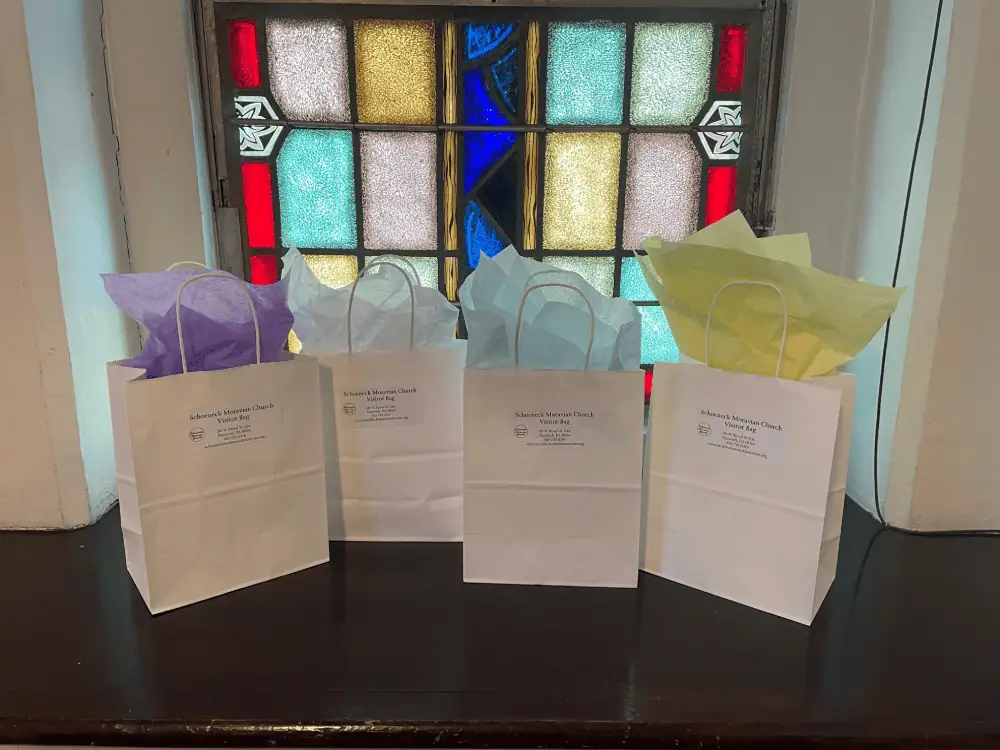 Four small white paper gift bags with colorful tissue paper siting out the top sit in a windowsill of one of the stained glass windows.