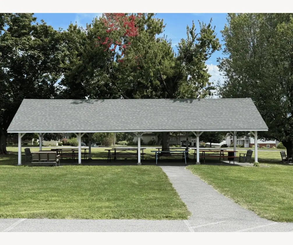 The Pavilion on a sunny day. The pavilion is surrounded on the far side by trees, and there are several picnic tables underneath. The Pavilion on a sunny day. The pavilion is surrounded on the far side by trees, and there are several picnic tables underneath.