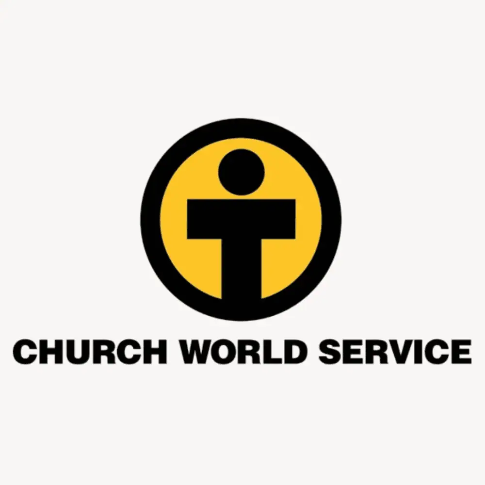 The logo for Church World Service features a golden yellow circle with a thick black ring around it. Inside the circle is a capital letter T with a circle above it as a rudimentary symbol of a human being. Underneath in a thick sans serif font are the words "Church World Service."