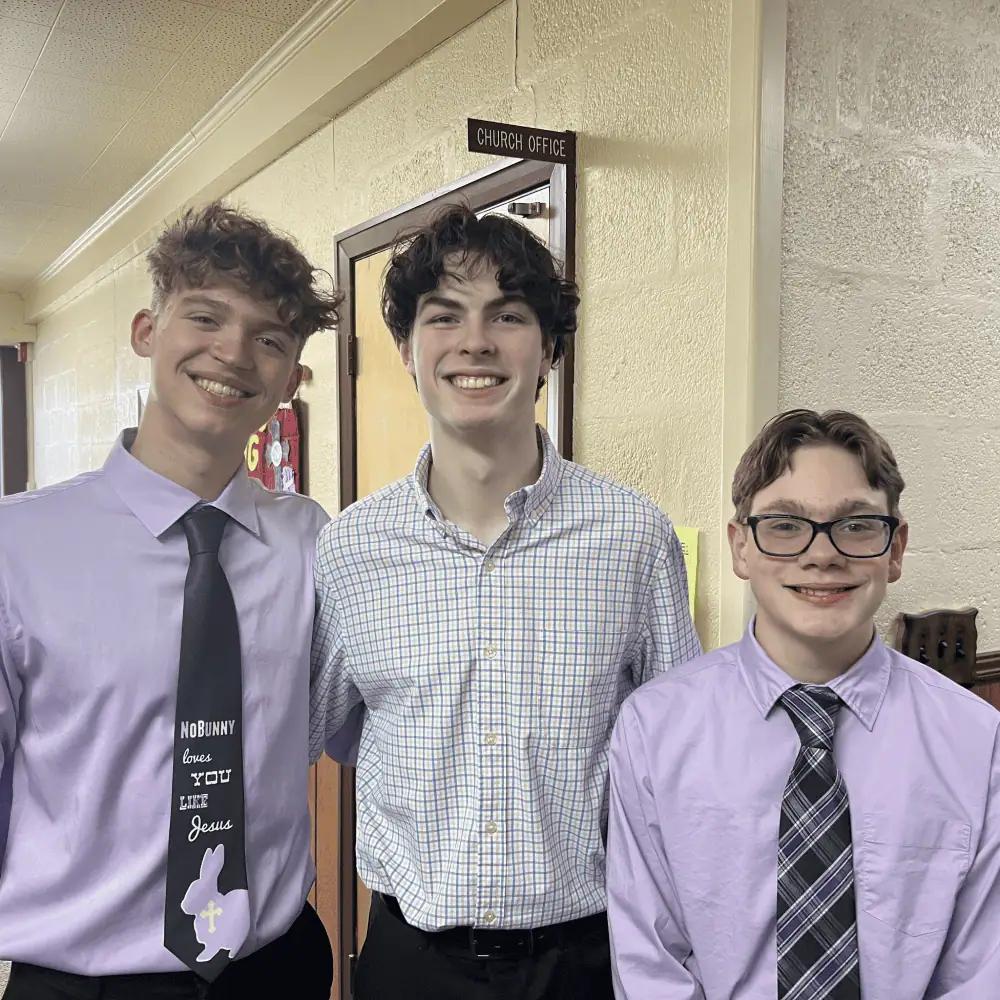 Three handsome young men wearing their Sunday best stand together on Easter Sunday. One of the young men's ties reads "No Bunny love YOU like Jesus."