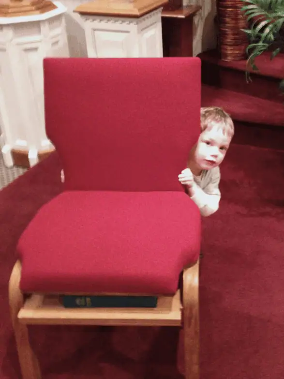 A young boy peeks around one of the chairs on the pulpit in the sanctuary.