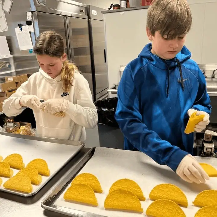 Two Schoeneckian teens, a girl and a boy, stack hard taco shells on baking sheets in the kitchen at Safe Harbor, Easton.