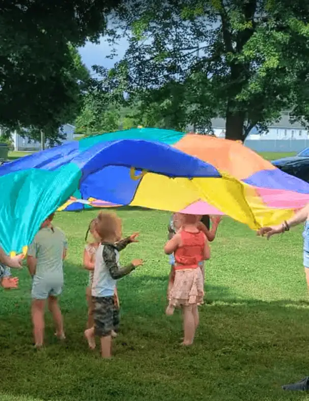 Several small children play under a colorful parachute in the grove during Vacation Bible School.