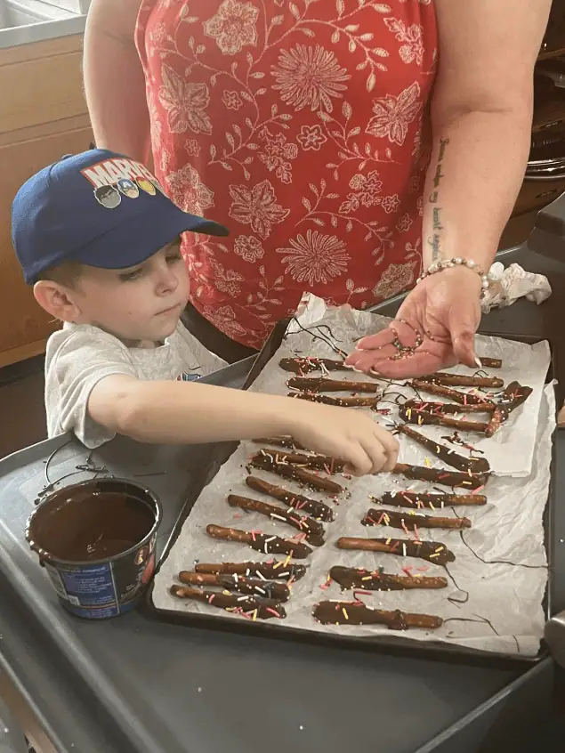 A young boy puts sprinkles on chocolate-dipped pretzel rods in the church kitchen.